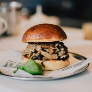 Delicious gourmet mushroom burger served with fresh sliced pickles on a plate.