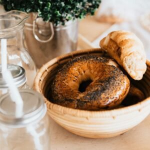 Fresh bagels and croissant on a wooden tray with mason jars, creating a warm rustic breakfast vibe.