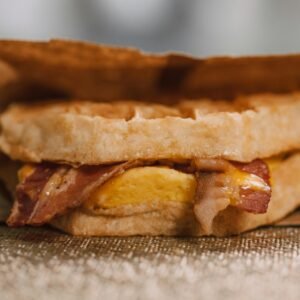 Mouthwatering waffle sandwich with bacon, egg, and cheese wrapped in paper.