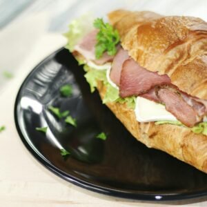 Tasty croissant sandwich with ham, cheese, and vegetables on a black plate.